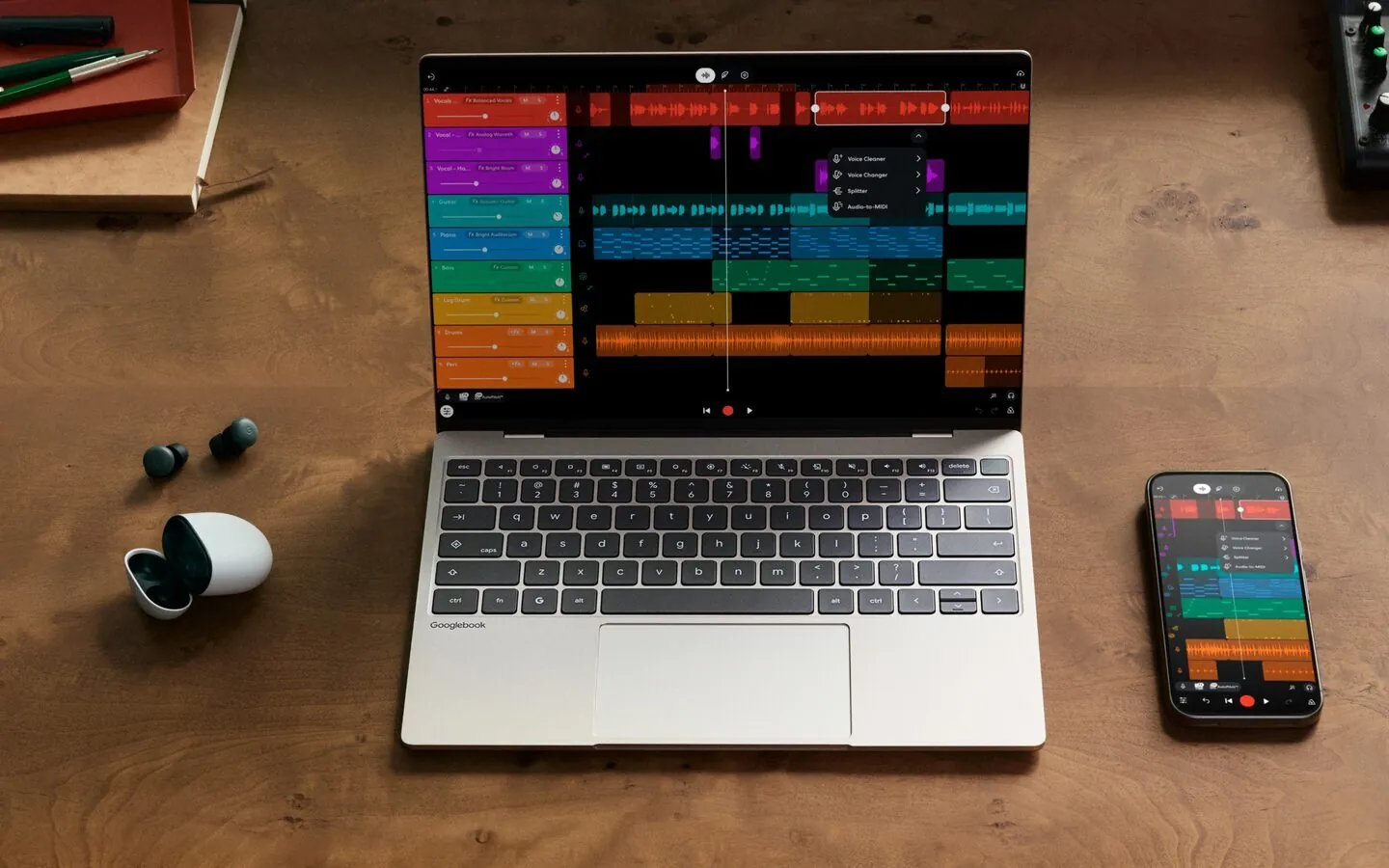Googlebook laptop open on a desk beside a phone and audio accessories