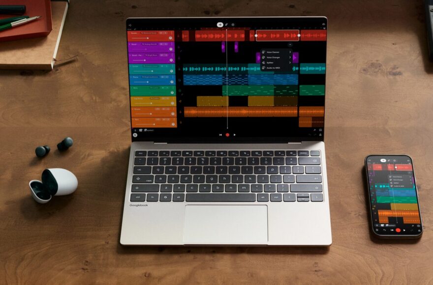 Googlebook laptop open on a desk beside a phone and audio accessories